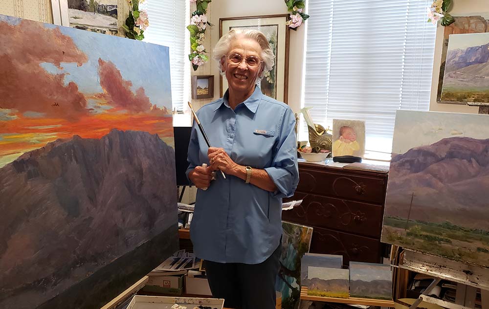 Woman artist in her studio standing next to one of her paintings