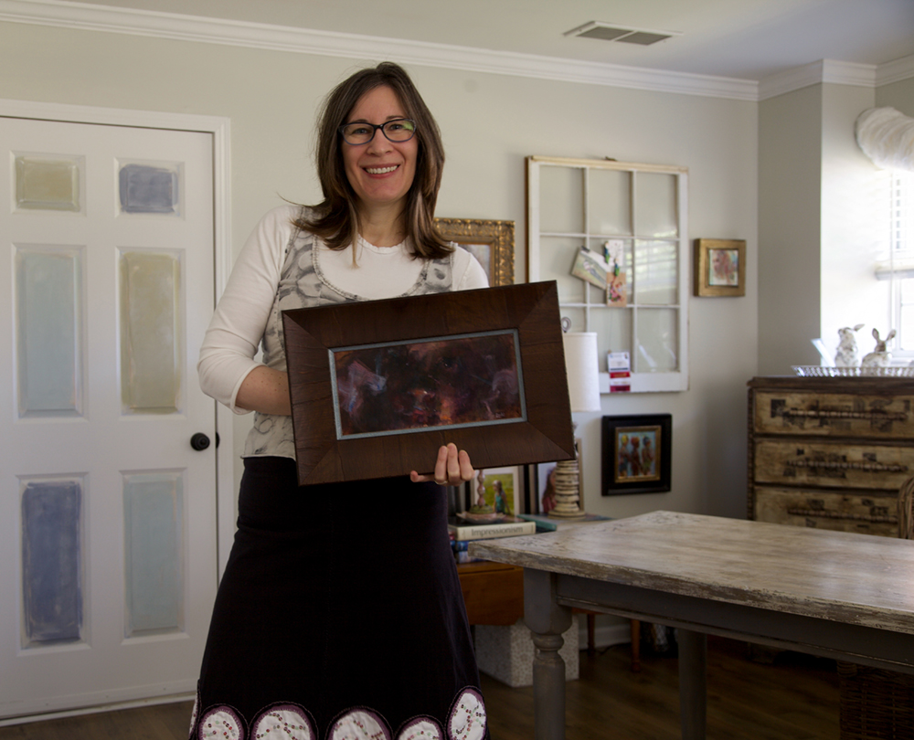 Woman artist in her studio holding a framed painting