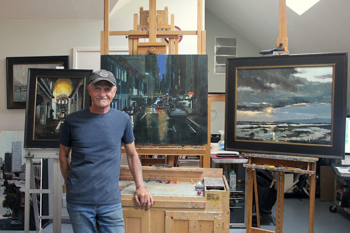 Male artist standing in his studio in front of his work on an easel