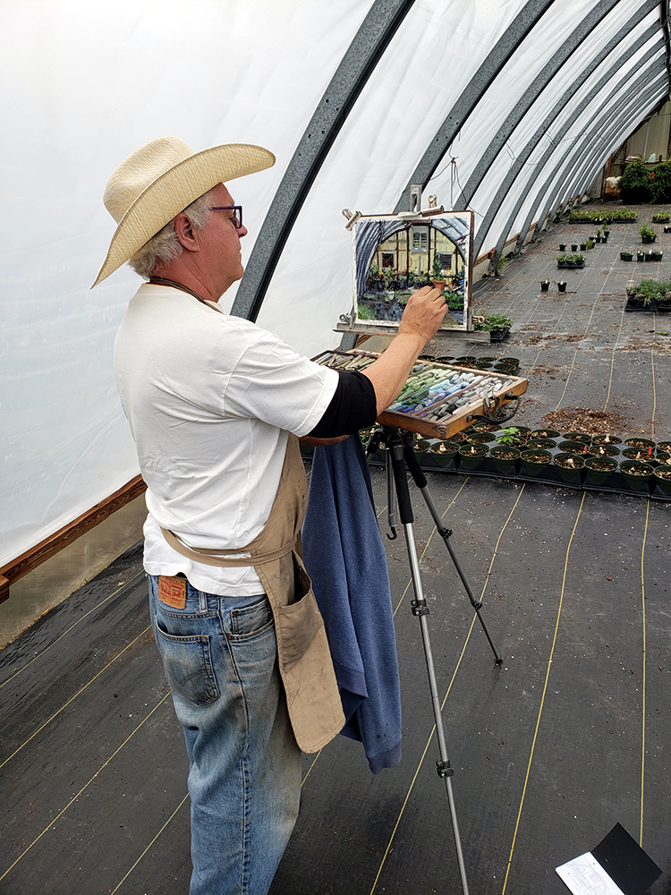Male artist in a cowboy hat painting on location at a nursery