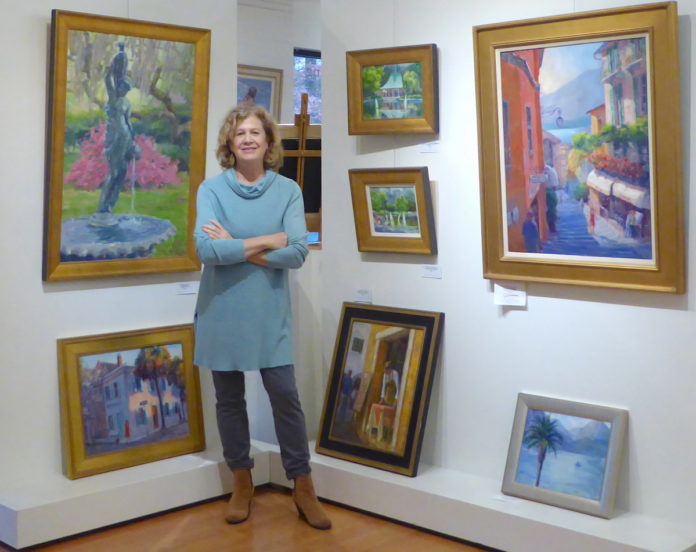 Female artist standing in front of her paintings in her gallery