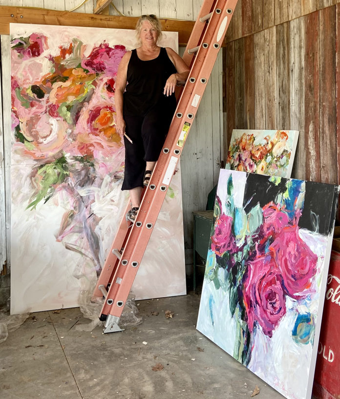 Female artist on ladder in front of her paintings