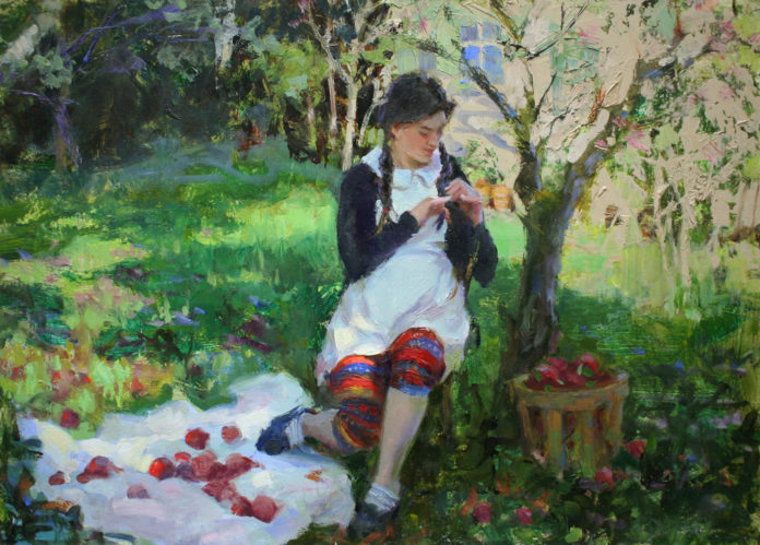girl sitting in a field next to tree, with picnic blanket and a basket full of red apples