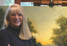 Artist Spotlight: Paula Holtzclaw Artist posing with her artwork, holding a paint brush