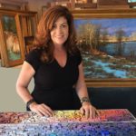 Artist Spotlight: Kim Lordier artist posing with her painting, touching the rainbow of pastels in front of her
