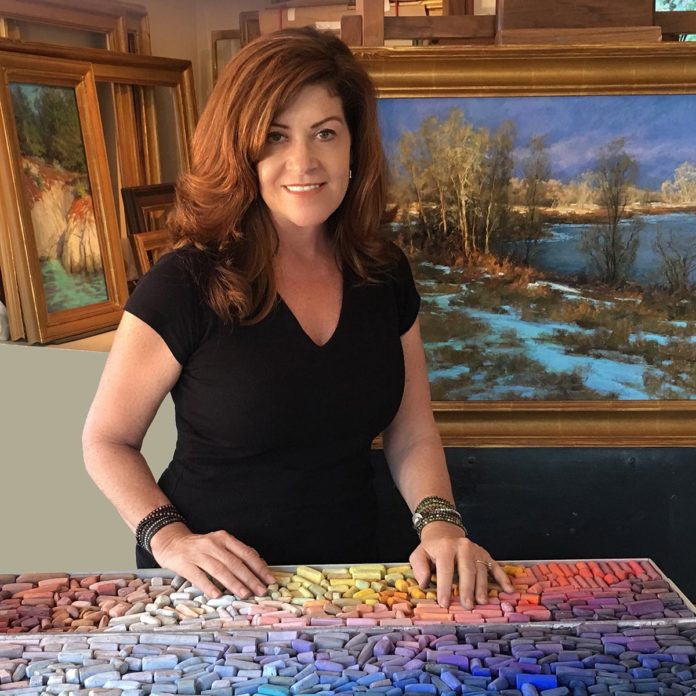 artist posing with her painting, touching the rainbow of pastels in front of her