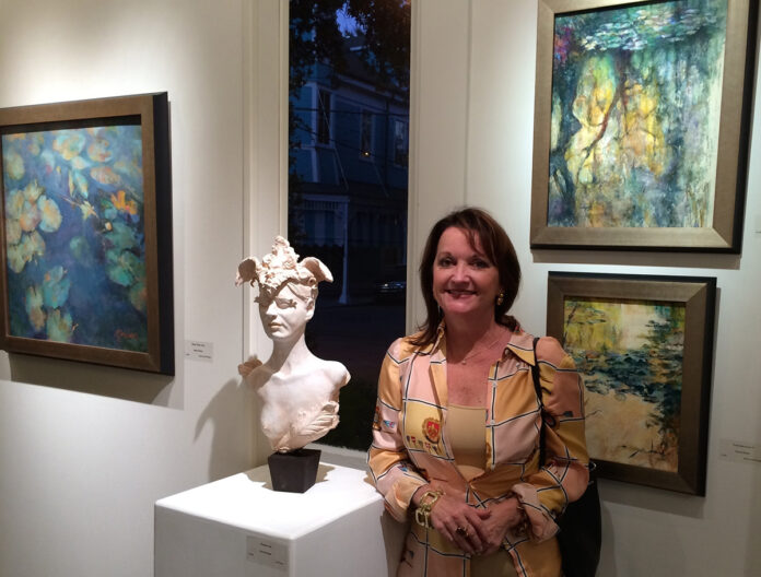 photo of artist standing in front of two paintings, and next to a head bust of a woman