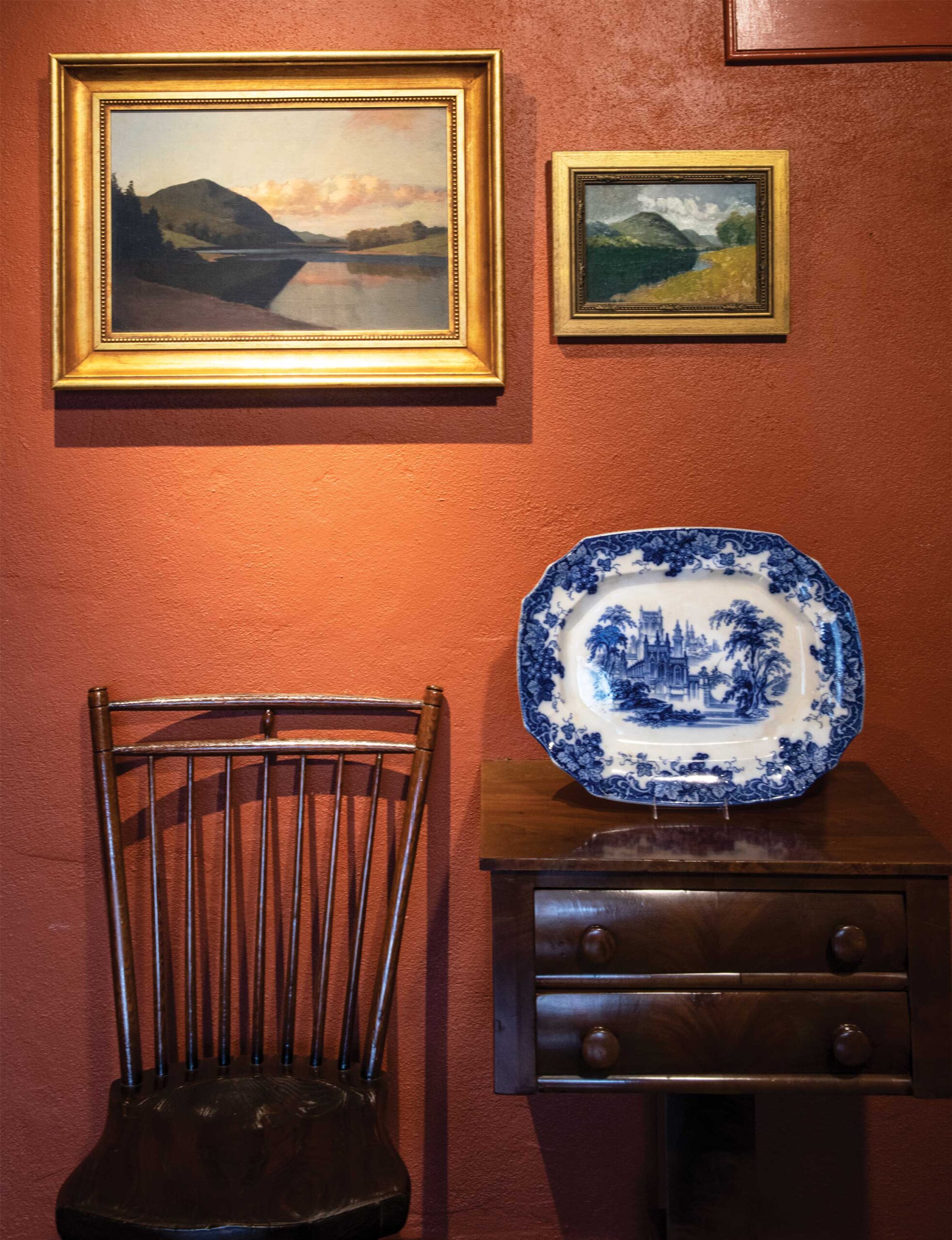 John F. Peto’s "Harper’s Ferry, West Virginia" (left) and "Study for Harper’s Ferry, West Virginia" hang above a vintage chair, heirloom blue-and-white platter, and antique side table.