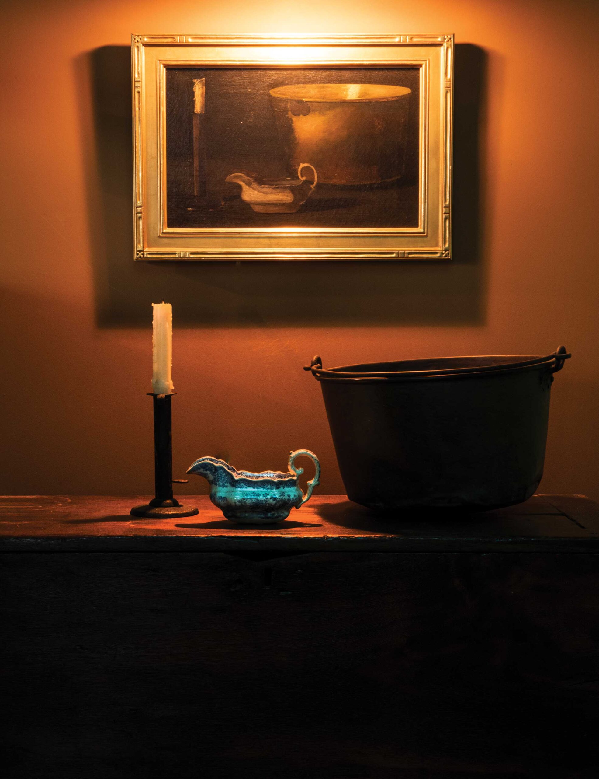 Peto’s painting "Brass Stewing Kettle, Candlestick, and Gravy Boat" (c. 1890) hangs above the original candlestick, gravy boat, and kettle that appear in it. 