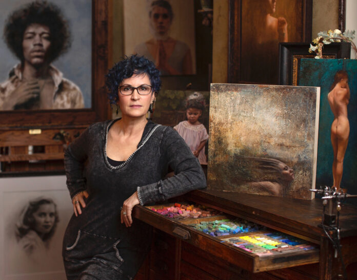 artist in her studio, with her paintings