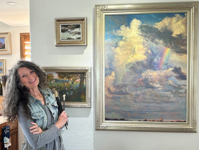 Karen at her home studio, posing with her paintings